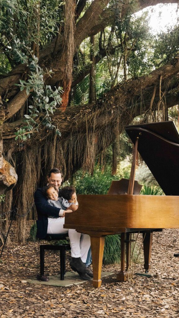 Dad holding kids at the grand piano in the Botanical Gardens.