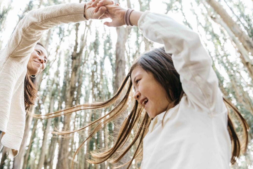 Mom twirling daughter around with eucalyptus trees towering in background.