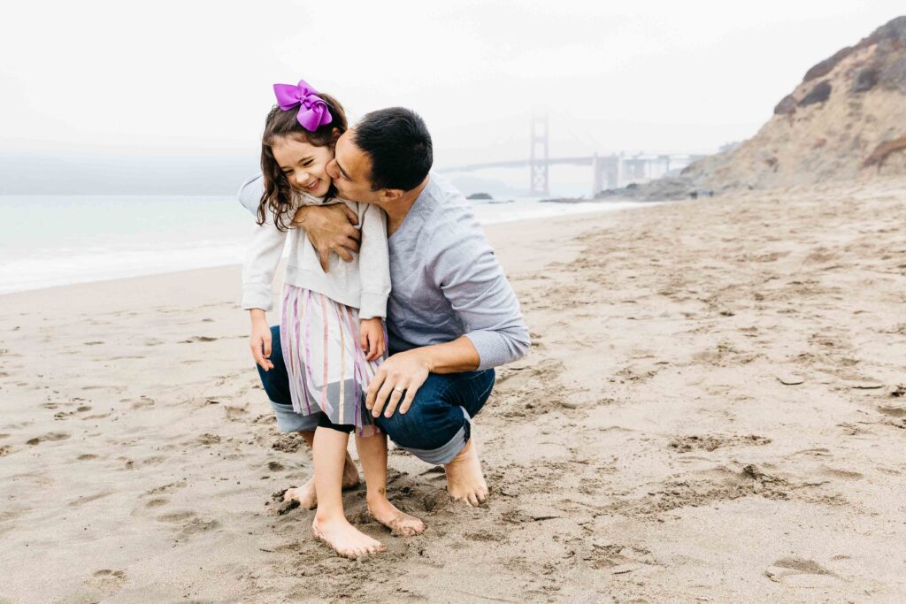 Dad kissing his young daughter at Baker Beach