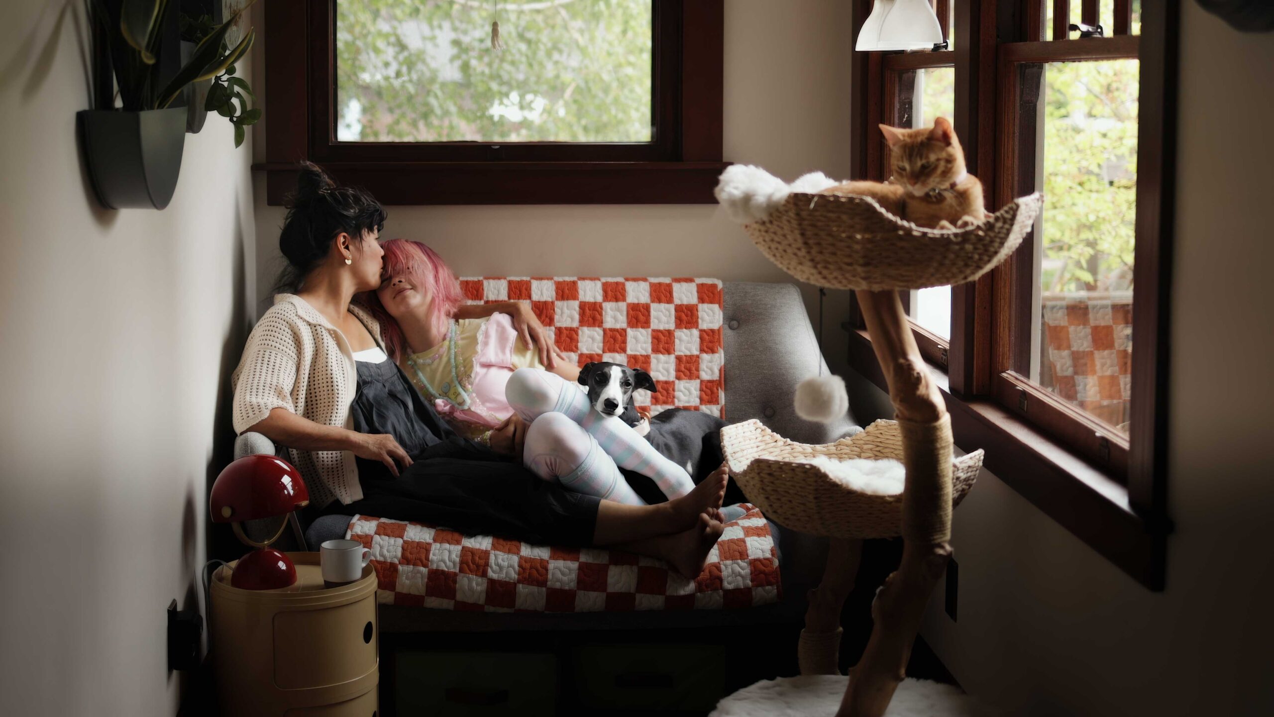 Mother kissing teen child on the loveseat with dog on her lap.