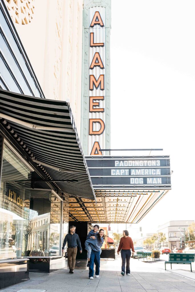 A family is walking under the theater marquee in downtown Alameda.