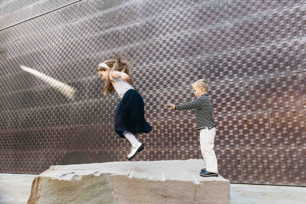 Sibling brother and sister jumping over rocks at the DeYoung Museum during a family photo session.