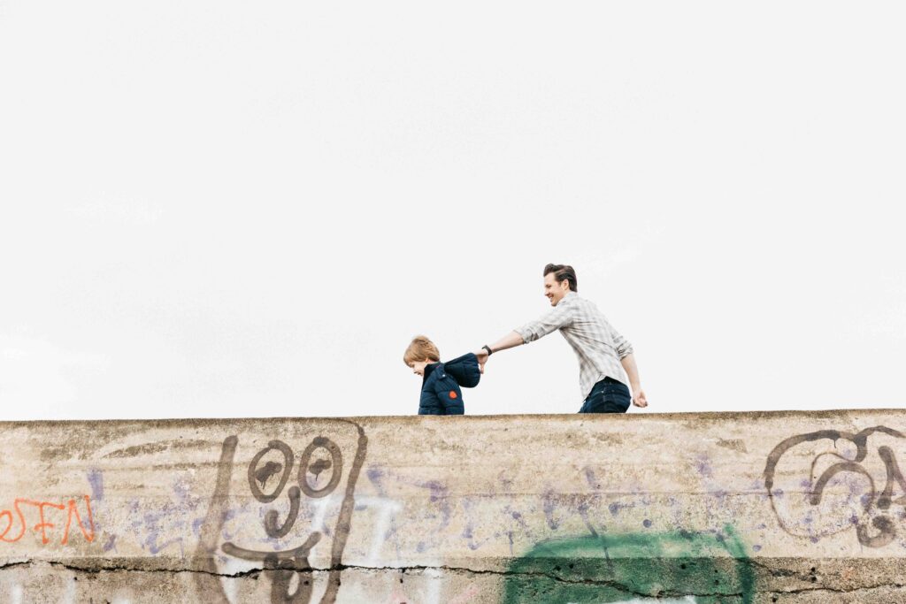 Dad grabbing toddler son by the hood of his jacket while walking at Battery Godfrey.