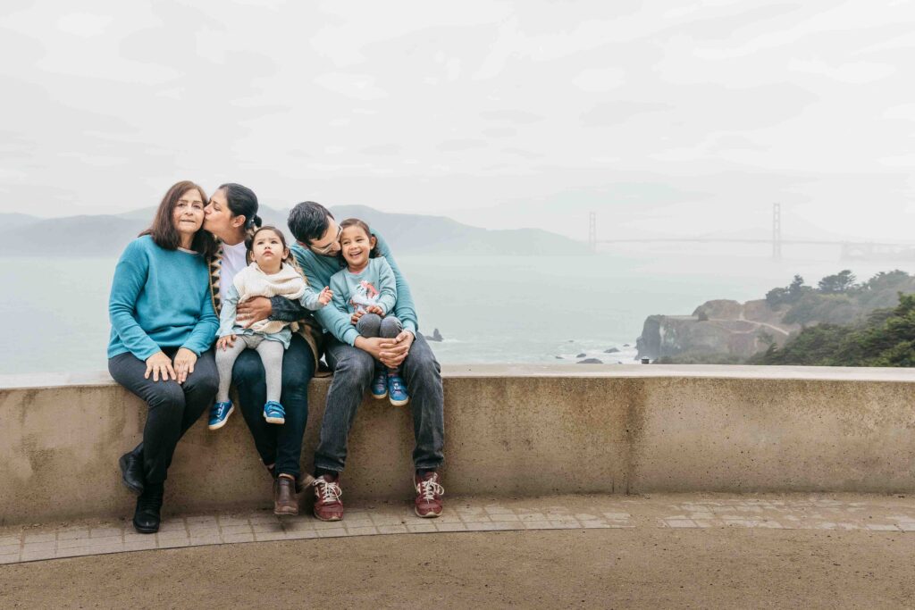 A family of of five is cuddling while sitting along a scenic overlook at Lands end.