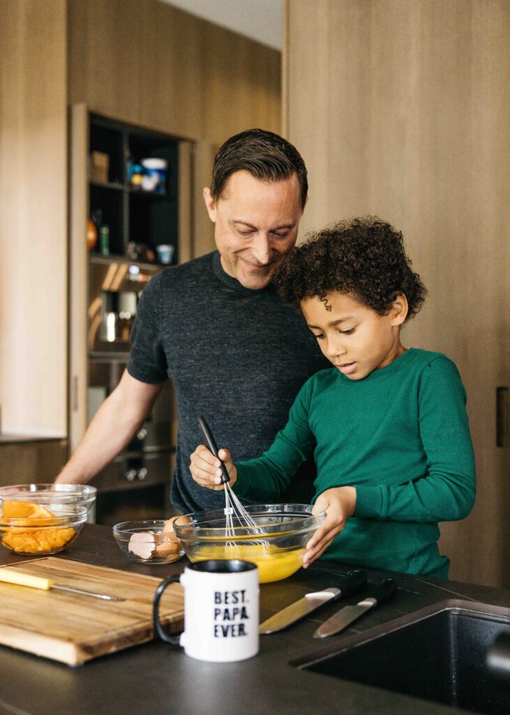 Dad is making a scrambled egg breakfast at home with his son.
