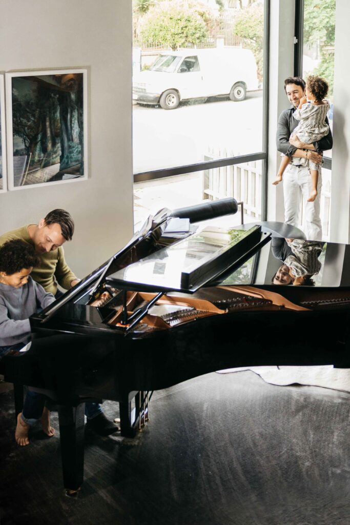 Dads playing the piano with their kids from their living room.