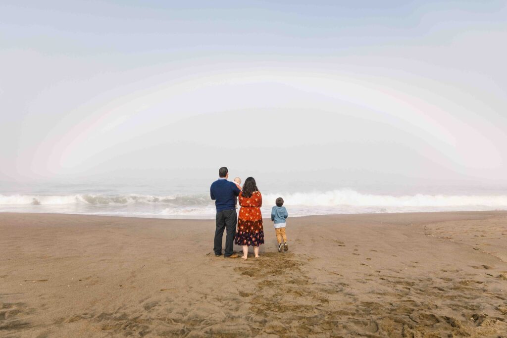 Family are standing along the shore with a rainbow in the sky.