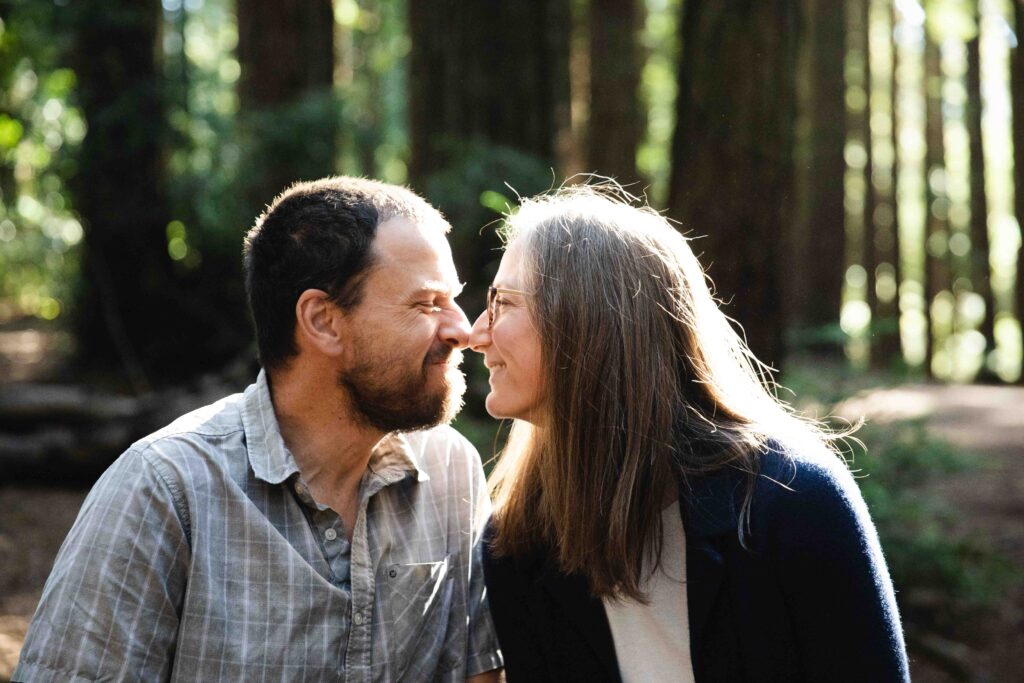 mom and dad are touching their nose tips at in a park.