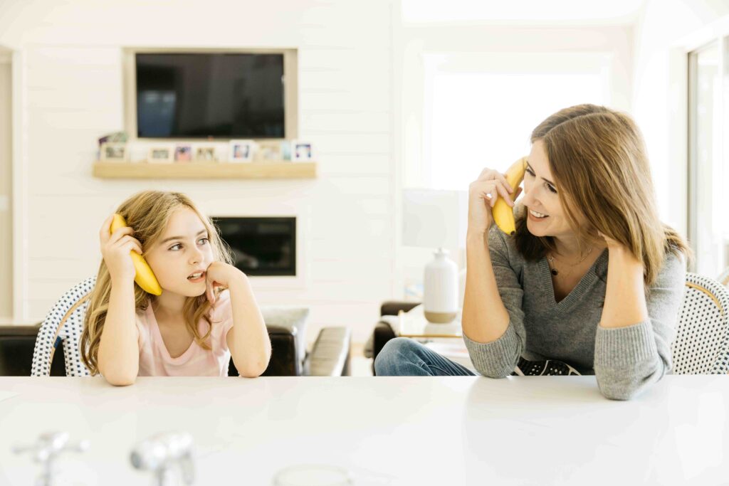 mom and daughter are pretending to talk to each other using a banana as a phone.