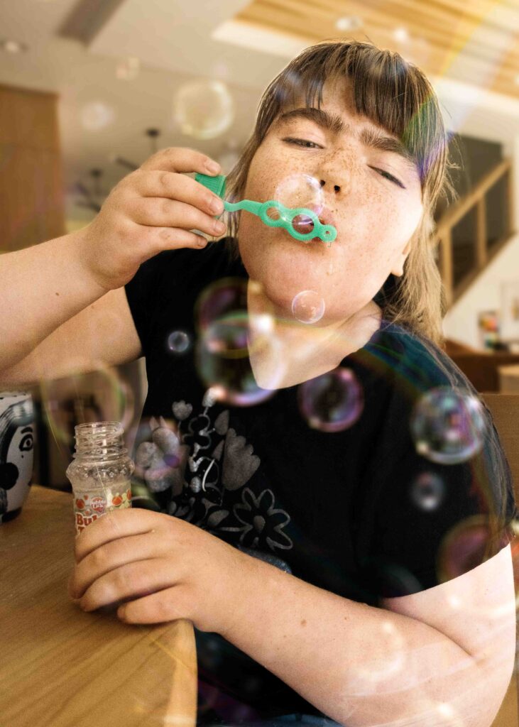 Girl is gently blowing bubbles from a wand at home.