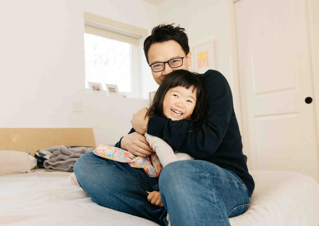 Dad is snuggling and hugging his daughter in the bed.