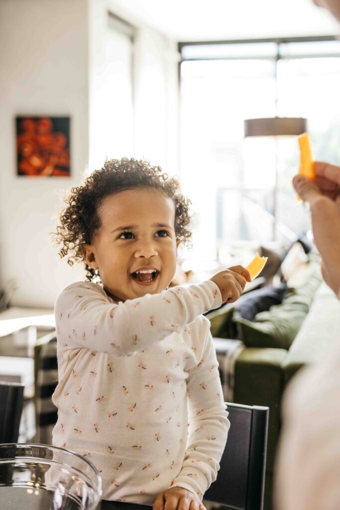 Daughter and dad are eating slices of cheese in the kitchen.
