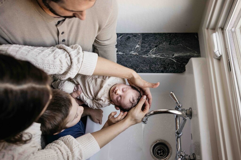 Family gently washes newborn baby in the sink.