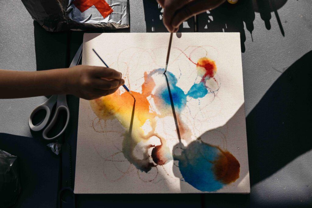 Mom and daughter are holding paint brushes as they apply watercolor on paper.