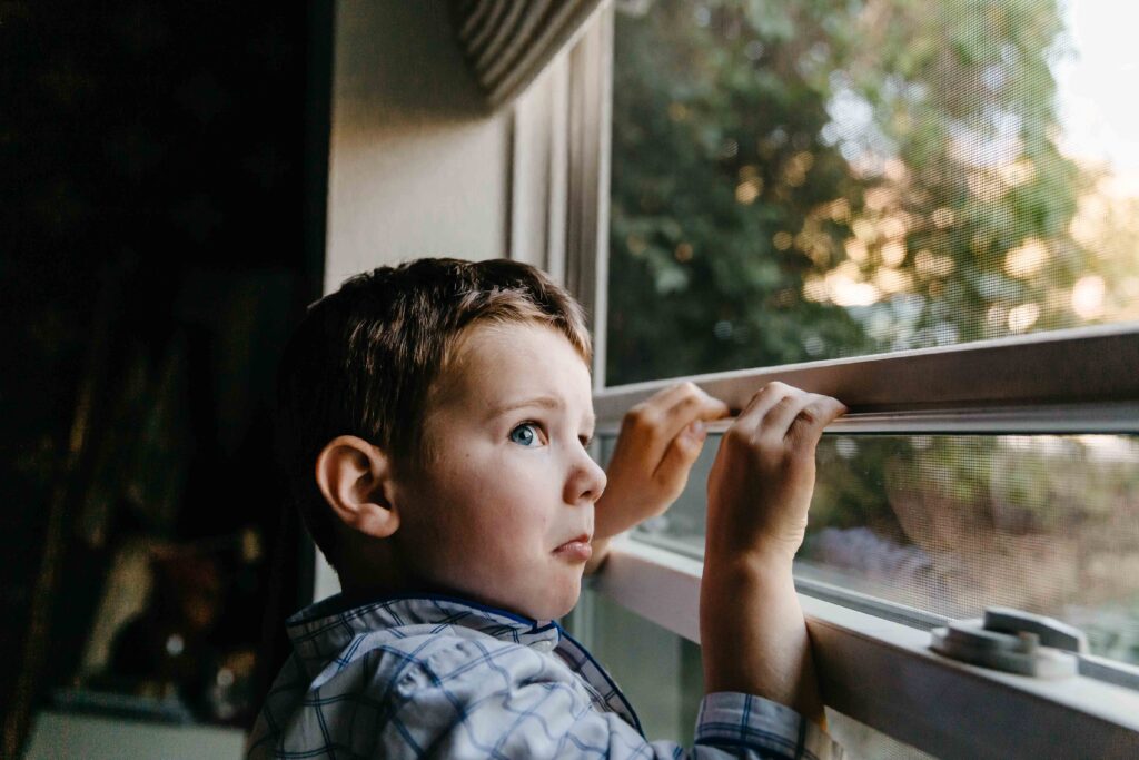 Young boy is balancing on a narrow window sill and making a precarious face.
