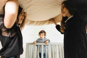 Younger brother watches his older sisters as they balance a pillow on their heads.