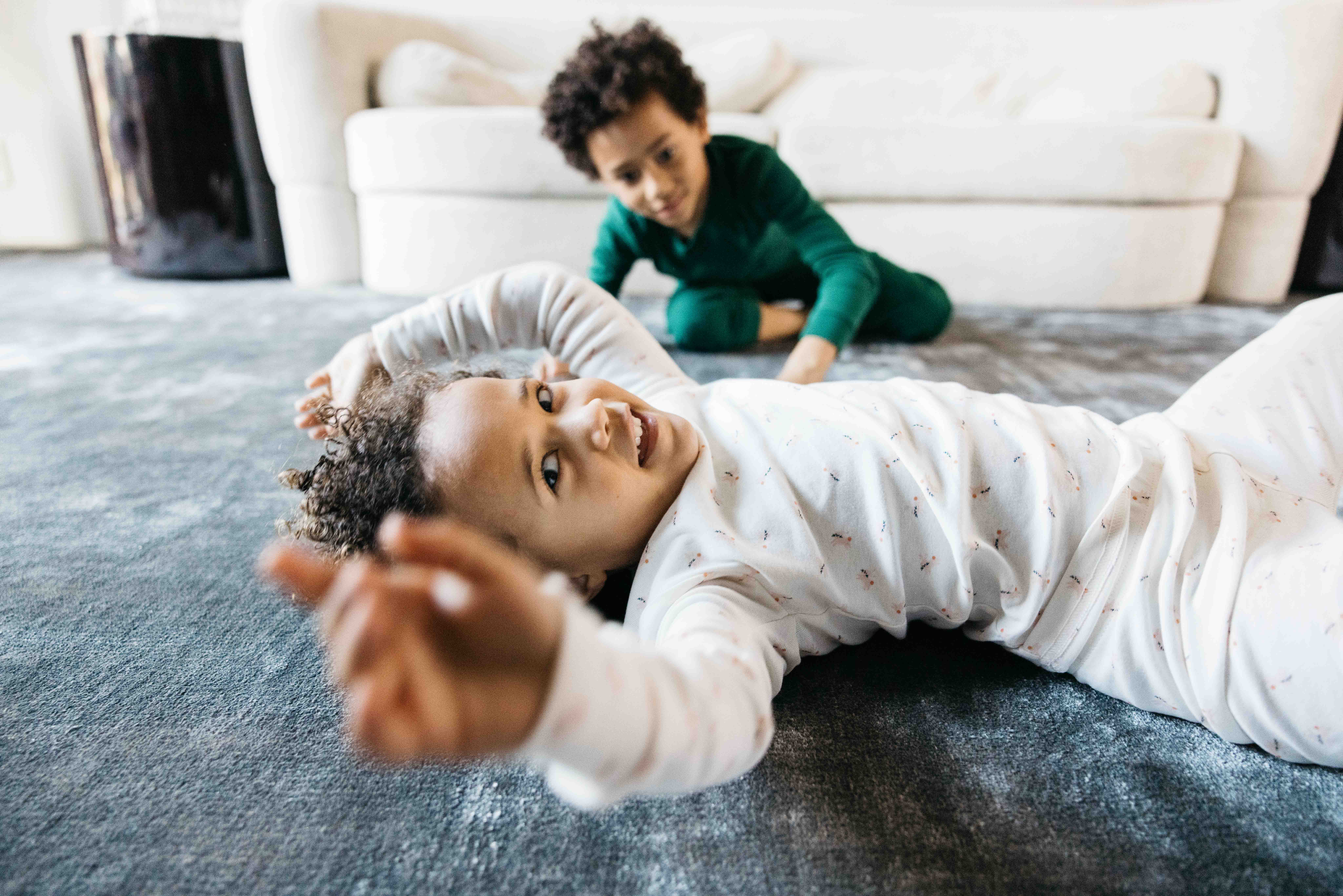 Toddler Siblings are having fun and rolling around the living room floor.
