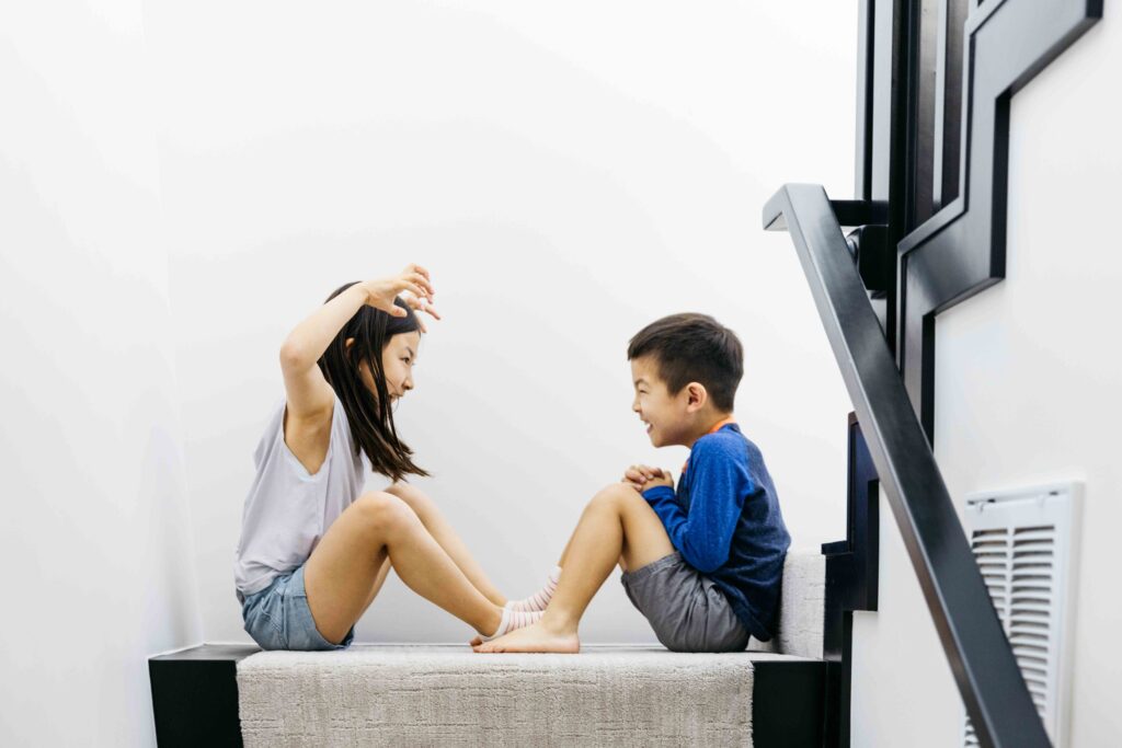 brother and sister are making funny faces at each other in the stairwell of their home.
