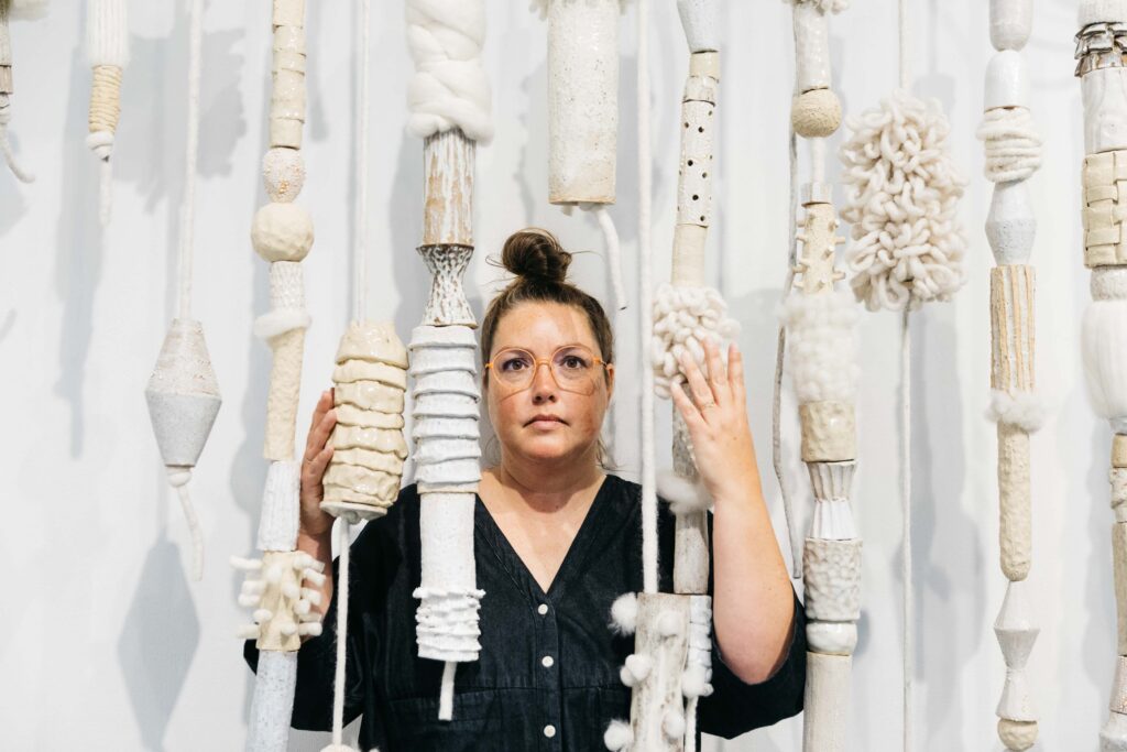 Ceramic artist and sculptor stands behind her large scale installment pieces during a branding photo session