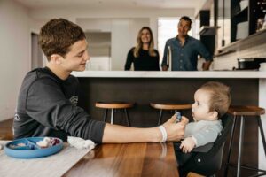Big brother is hand feeding his baby brother some food puree.