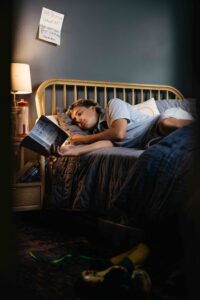 Teen boy is reading a paperback book in his bedroom.