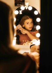 teen girl is brushing her hair in front of her vanity mirror during a family photo session at home.