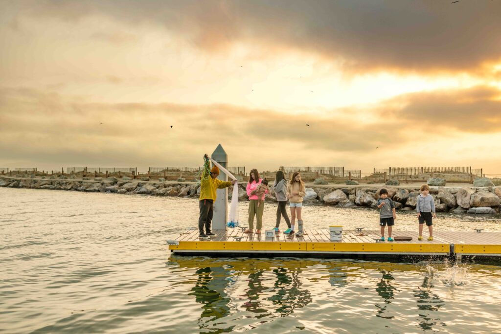 A blended family is fishing on the pier during sunset.