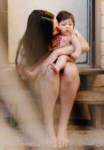 Mom is kissing her baby girl on the cheek during a newborn session at home.