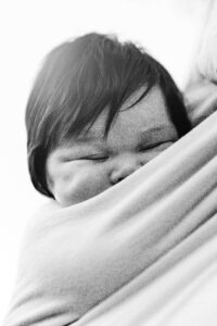 Newborn baby girl is sleeping soundly in a baby carrier against her mother's chest.