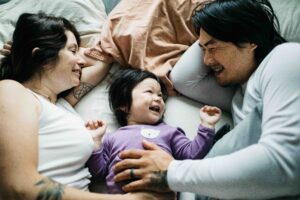 Newborn baby girl snuggling and smiling with mom and dad in bed.
