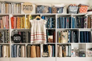 Vintage embroided dress hangs on fabric wall of vintage fabric bolts.