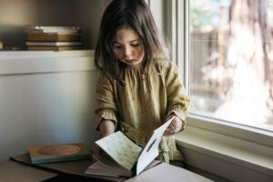 Young toddler girl is flipping through the pages of a hardcover book at home.