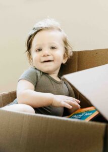 Baby brother is playing in a box full of books.