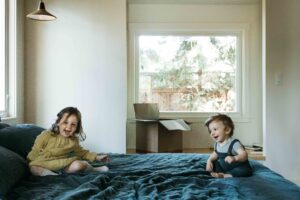 Sibling brother and sister are laughing on the bed.