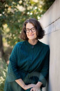 Therapist is smiling at the camera as she leans naturally against a wall during a headshot session in Berkeley.