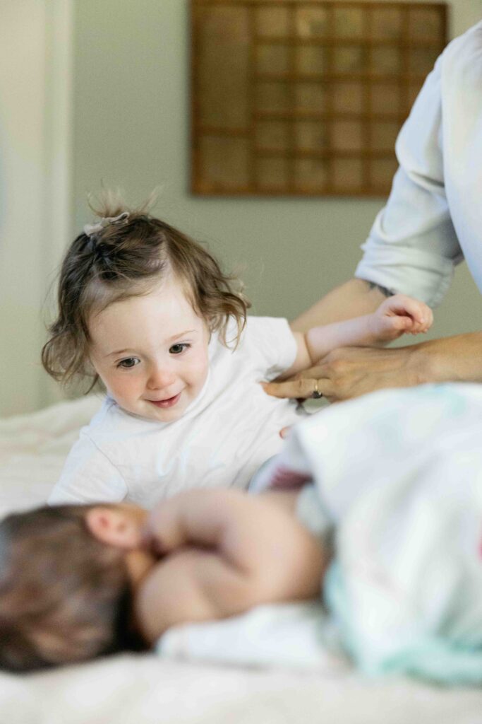 older sibling sister is playing with baby brother during a newborn photo session in san francisco.