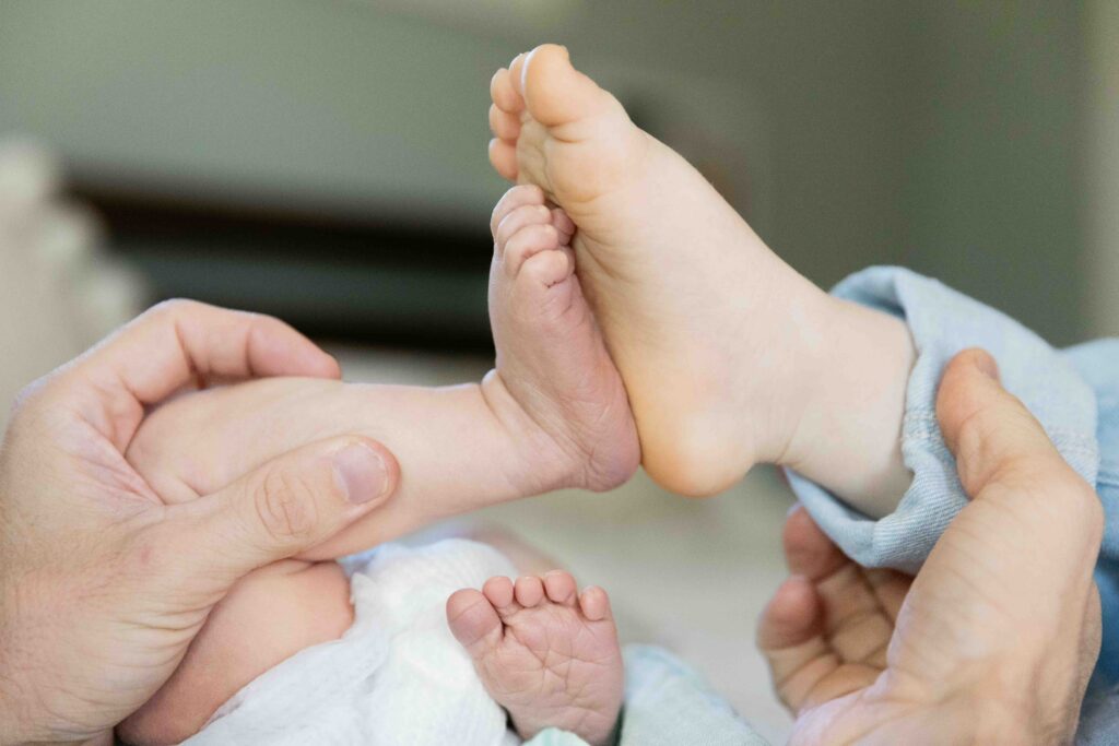 Older sister and newborn baby brother are pressing their feet together during a newborn photo session.