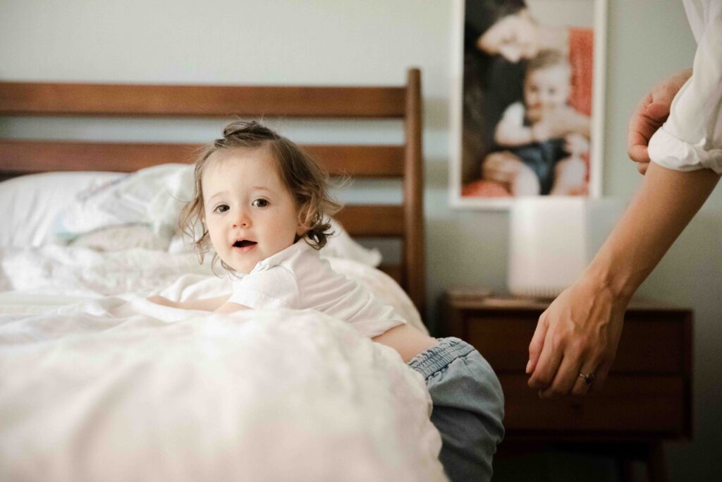 Older sibling sister is climbing on the bed during a family photo session at home.
