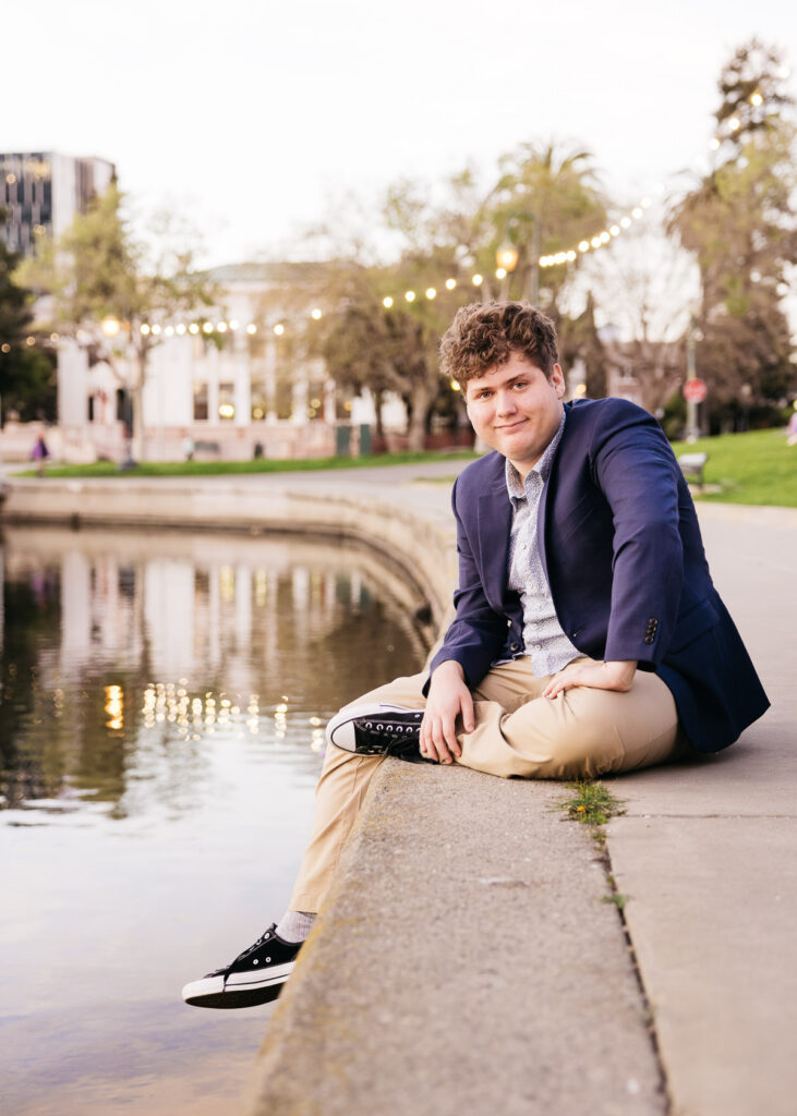 High school senior is sitting at Lake Merritt at sunset during a senior photo session.