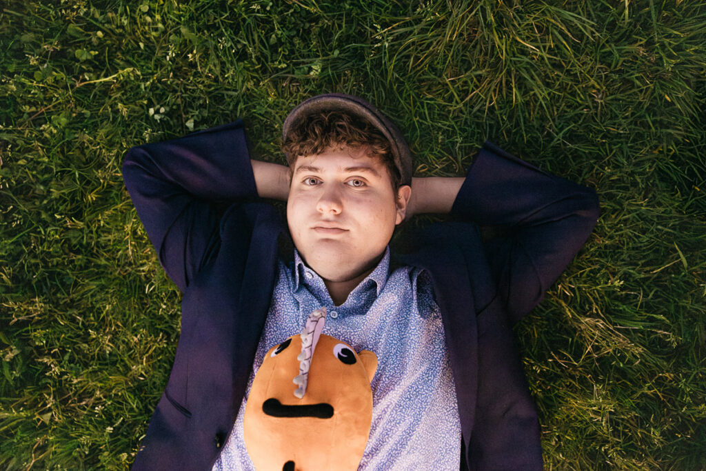 Senior grad is laying on the grass gazing at the sky with his favorite stuffed animal during a senior photo session.