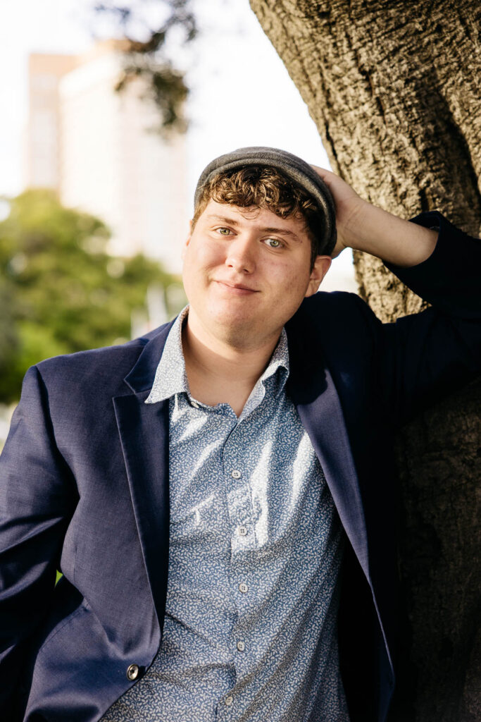 High school senior grad is leaning against a tree and smiling at Lake Merritt during his senior photo session.