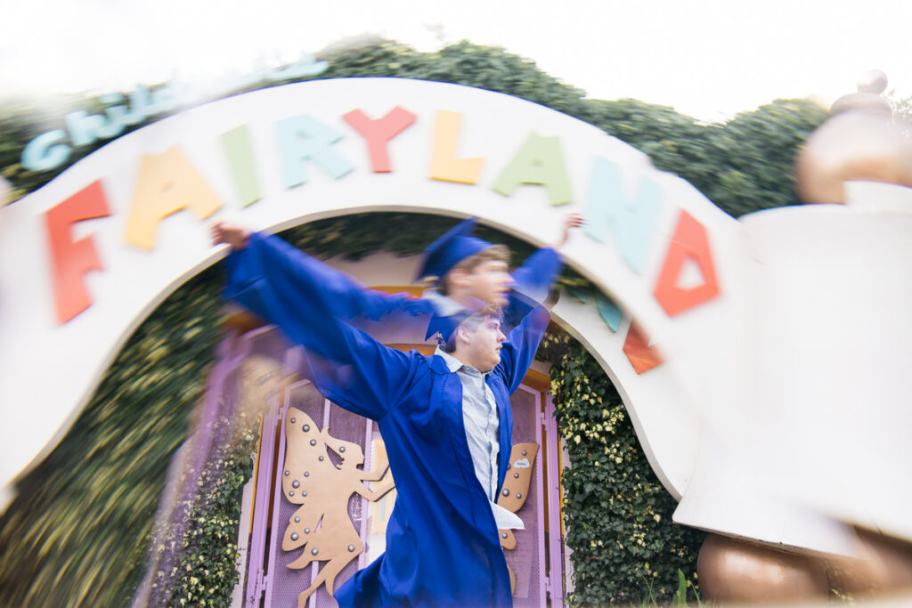 Senior high school grad is skipping at the gates of Fairyland during his senior photo session.
