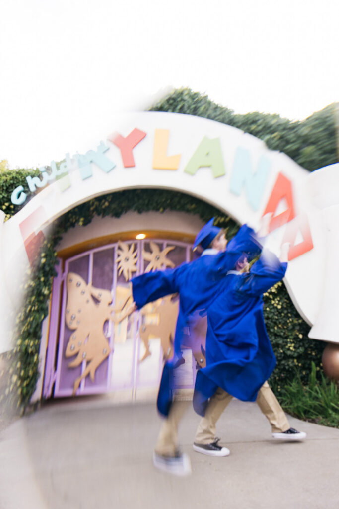 Senior high school grad is skipping at the gates of Fairyland during his senior photo session.