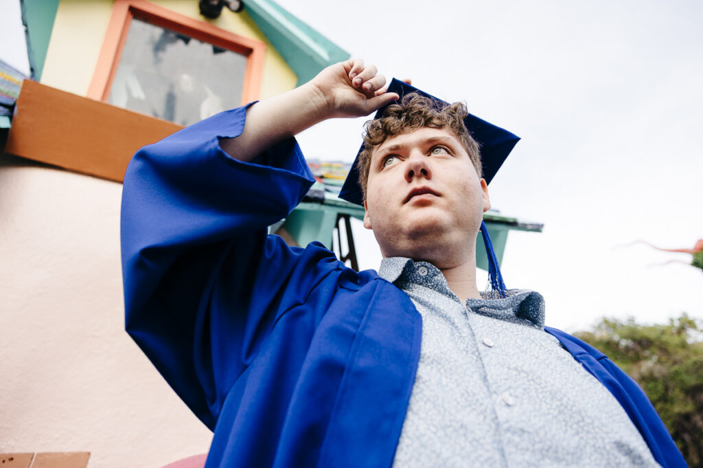 High school senior is adjusting his cap while wearing his graduation gown at the gates of Fairyland.