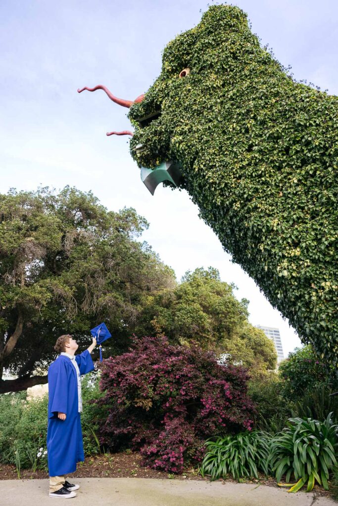 Senior grad is waving his cap to the dragon at the Fairyland gates during his senior photo session.