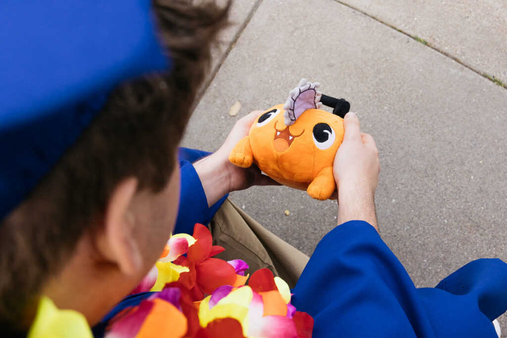 Senior high school grad is hugging Pochita while wearing his cap and gown during his photo session.