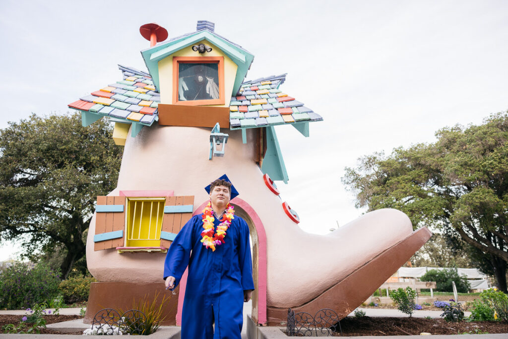 Senior grad is smiling while wearing his cap and gown at his photo session at Fairyland.