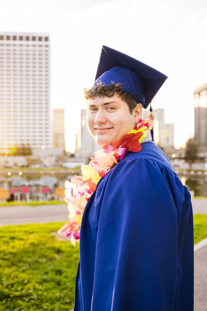 High school graduate is wearing his cap and gown and smiling at Lake Merritt during his senior photo session.