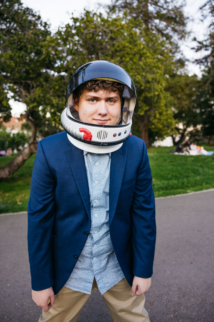 High school senior is wearing a suit and jacket with astronaut helmet during his senior photo session in Oakland.