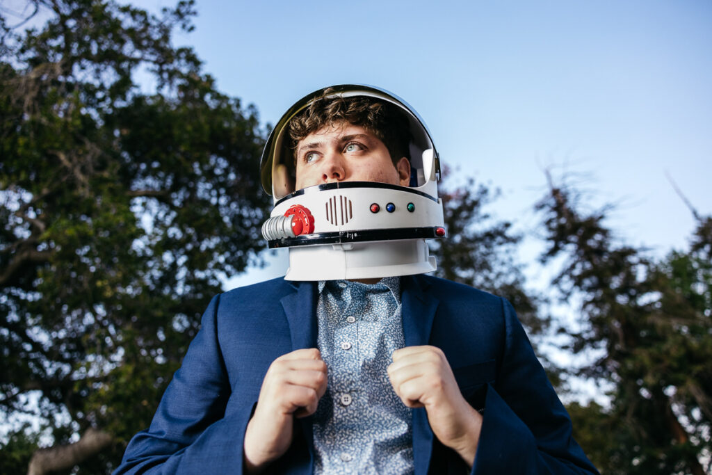 High school senior is wearing a suit and jacket with astronaut helmet during his senior photo session.